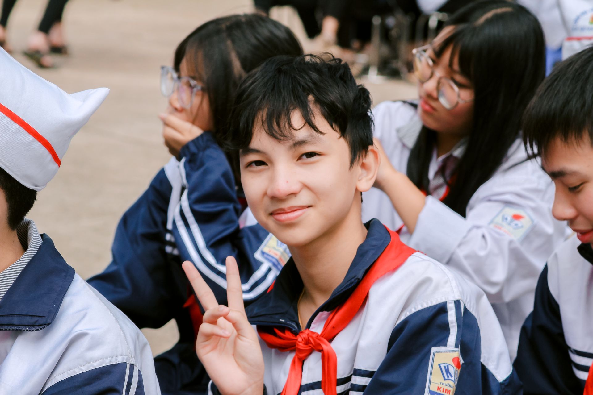 The bright smile of a young boy holding a peace sign, surrounded by his fellow classmates.